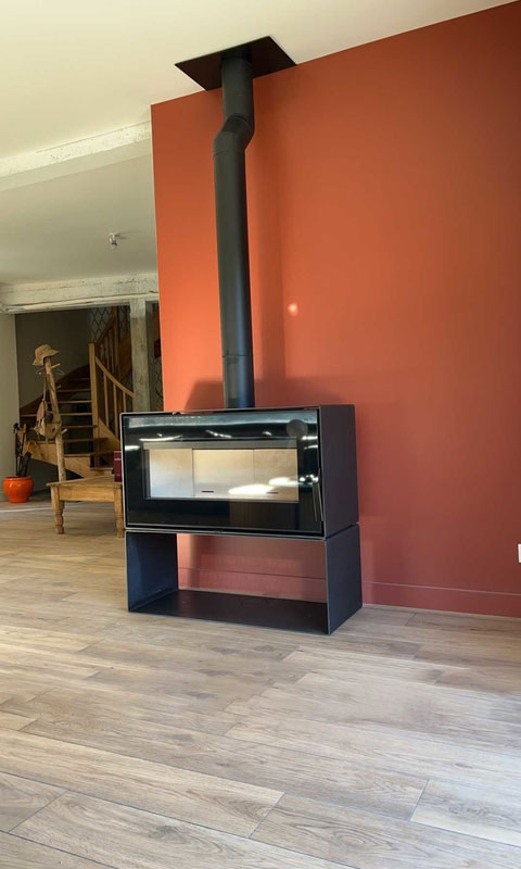 Poêle moderne Cheminées des Pyrénées à Séméac, installé dans un salon chaleureux avec parquet bois et mur rouge brique,