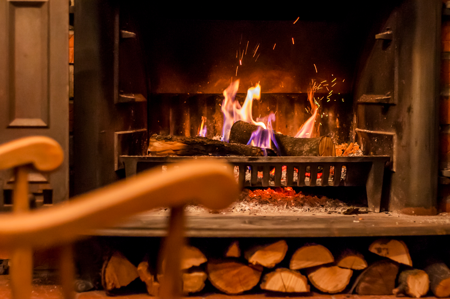 Ambiance chaleureuse devant une cheminée allumée Cheminées des Pyrénées à Séméac avec fauteuil en bois,